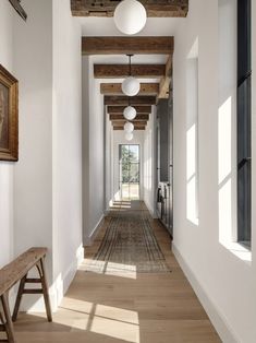 a long hallway with white walls and wooden beams on the ceiling is flanked by two benches