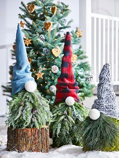 three gnome hats sitting next to a christmas tree in the middle of snow covered ground