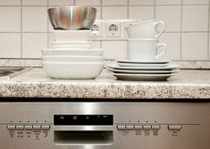 dishes and cups are stacked on top of the dishwasher's control panel