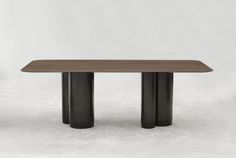 a wooden table with two black legs and a white wall in the backround