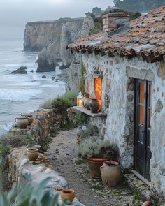 an old stone house next to the ocean with potted plants and lights on it