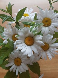 a vase filled with white and yellow flowers on top of a wooden table next to leaves