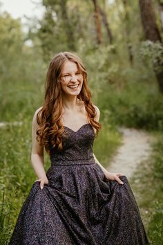 a woman in a dress is posing for a photo by some trees and grass with her hands on her hips