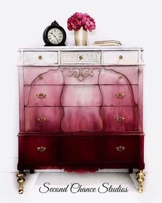 a pink dresser with flowers and a clock on it's top, in front of a white wall