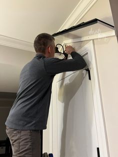 a man working on a door handle in a room with white walls and black trim