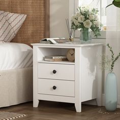 a white nightstand with flowers on it next to a bed