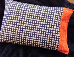 a blue and white pillow with an orange patch on the front side, sitting on a black blanket