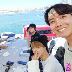 three young men sitting at a table with cell phones on it and water in the background