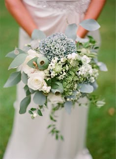 a bride holding a bouquet of white and blue flowers on her wedding day in the grass