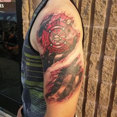 a man with a firefighter's tattoo on his arm is standing in front of a brick wall