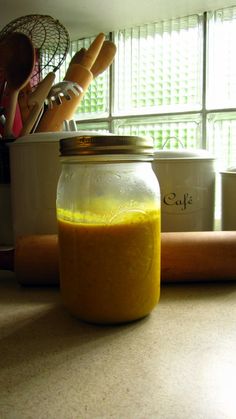 a jar filled with yellow liquid sitting on top of a counter next to some bread