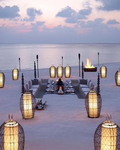 an outdoor dining area on the beach with lanterns lit up at night and water in the background