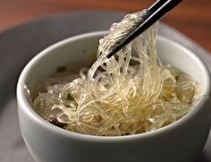 chopsticks are being used to stir noodles in a white bowl on a gray plate