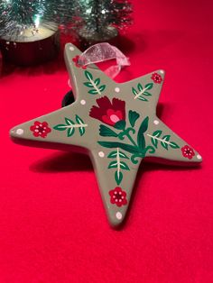 a green star shaped ornament with red flowers and leaves painted on it sitting next to a christmas tree