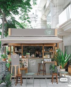 an outdoor cafe with tables and stools in front of the counter, surrounded by greenery