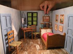 a doll house with furniture and pictures on the walls, including a bed in between two windows