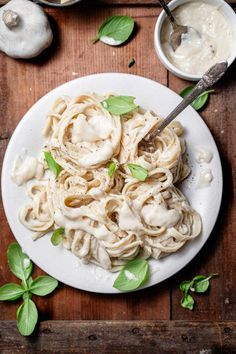 a white plate topped with pasta covered in sauce and basil next to two bowls of mushrooms