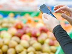 a woman is using her cell phone in front of an assortment of fruits and vegetables