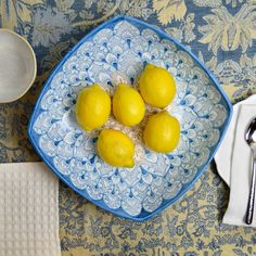 four lemons in a blue and white bowl on a floral tablecloth with silverware