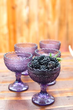 purple glass goblets filled with blackberries on a wooden table