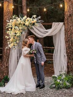 a bride and groom kissing in front of an outdoor wedding arch with flowers on it