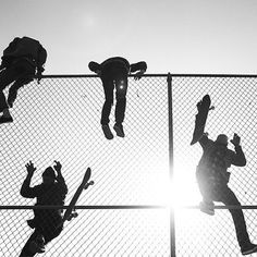 silhouettes of skateboarders jumping over a fence