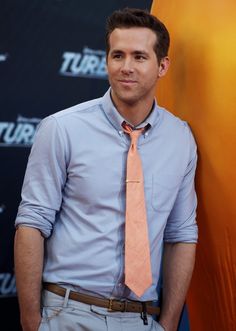 a man in a blue shirt and orange tie standing next to a yellow surfboard