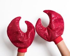 pair of red sequined gloves held up by two hands, on white background