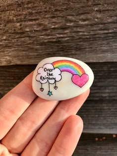 a hand holding a white rock with a rainbow and heart on it that says over the rainbow