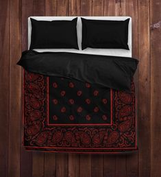 a bed with black and red comforters on top of wooden floor next to wall