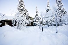 a sign in the snow near some trees and a building with a restaurant on it