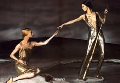 two women dressed in gold pose for the camera, one holding an umbrella while the other holds her hand