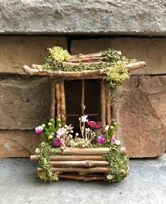 a small window made out of sticks with flowers in the windowsill and moss growing on it