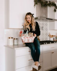 a woman sitting on top of a kitchen counter holding a basket filled with food and ice cream