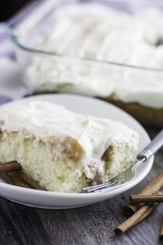 a piece of cake with white frosting on a plate and cinnamon sticks next to it