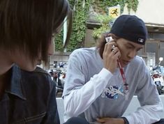 two people sitting on the ground talking on cell phones and one is holding a phone to his ear