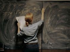 a woman writing on a blackboard in front of two chalkboards with writing on them