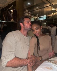 a man and woman sitting at a table with food in front of them, posing for the camera