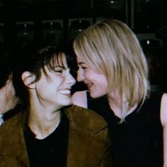 two women are smiling and laughing at each other's sides while one woman is wearing a brown jacket