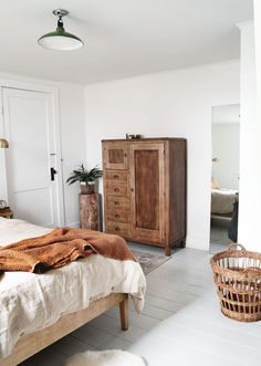 a bed room with a neatly made bed next to a wooden dresser and basket on the floor