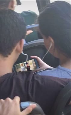 two people sitting on a bus and one is holding a cell phone while the other holds a camera