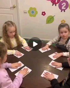 several children sitting around a table playing with paper and glue on the top of it