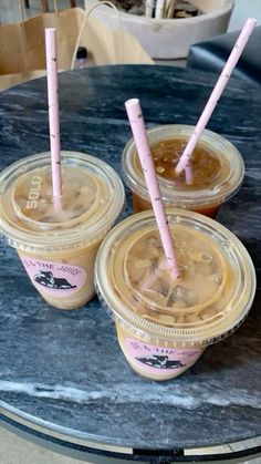 three cups filled with liquid sitting on top of a table next to two pink straws