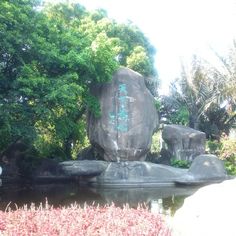 a large rock sitting in the middle of a pond surrounded by lush green trees and bushes