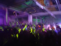 a large group of people dancing in a room with purple and green lights on the ceiling