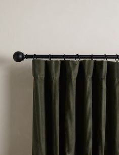 a curtain hanging on a black rod in front of a white wall with green striped curtains