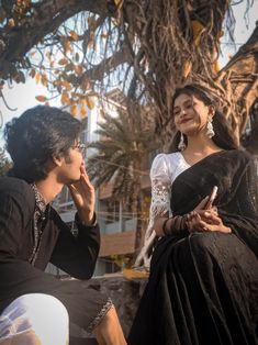 a man and woman sitting next to each other under a tree