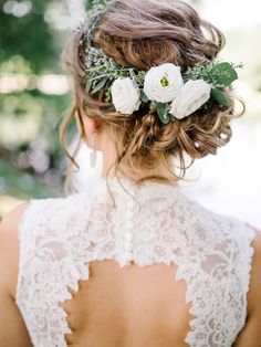 the back of a woman's head with flowers in her hair and greenery