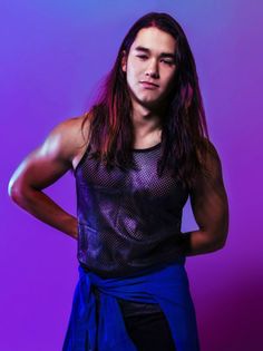 a man with long hair standing in front of a purple and blue background wearing a tank top