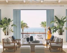 a woman standing in front of an open window looking out at the ocean and palm trees